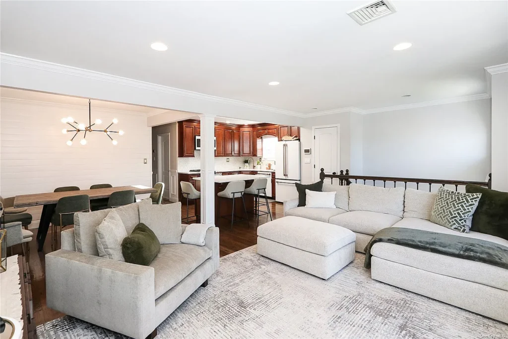 Open concept living, dining, and kitchen layout with a large neutral linen sectional sofa, green accent pillows, sputnik chandelier over dining area, cherry wood kitchen cabinets, and hardwood floors